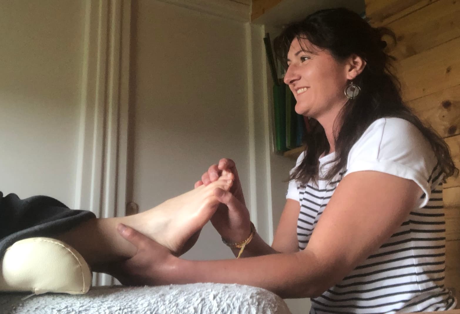 Julie Viandier en séance de réflexologie plantaire, t-shirt rayé, mains posées sur le pied d'une cliente.